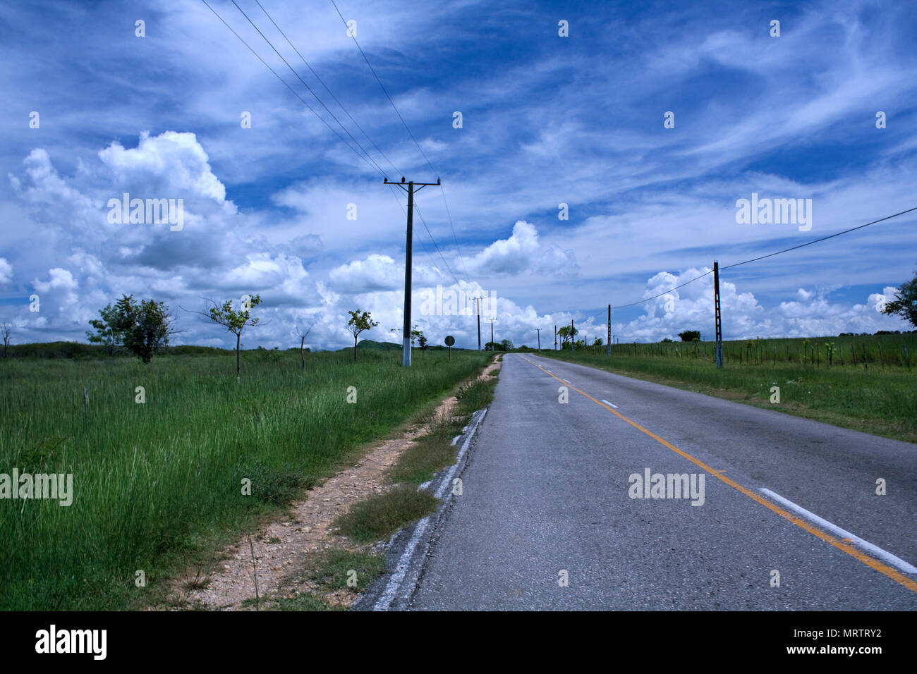 Electricity poles standing near narrow road going through green fields of countryside in Trinidad, Cuba. Stock Photo