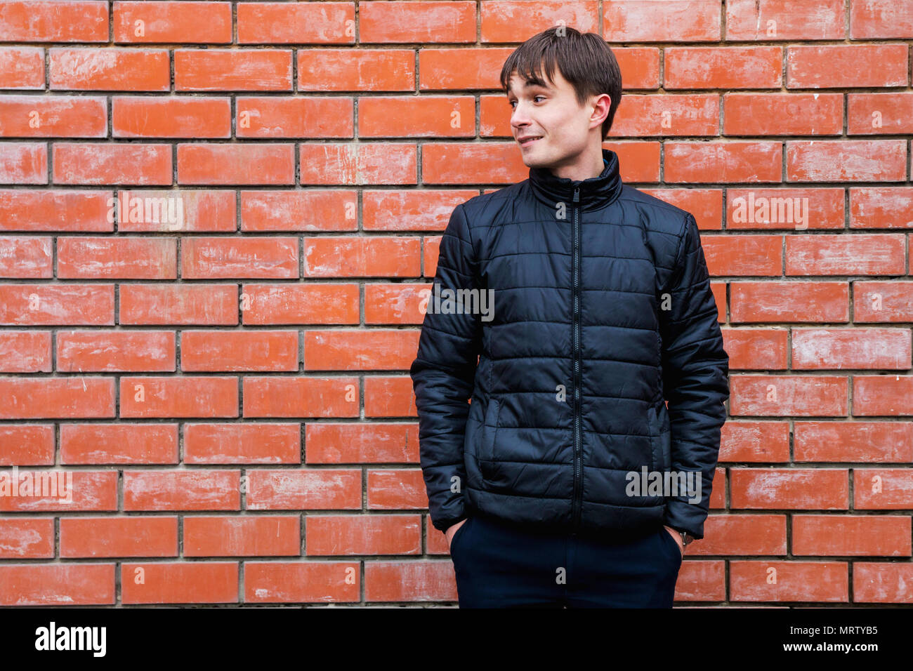 a young man stands leaning against a brick wall. Stock Photo