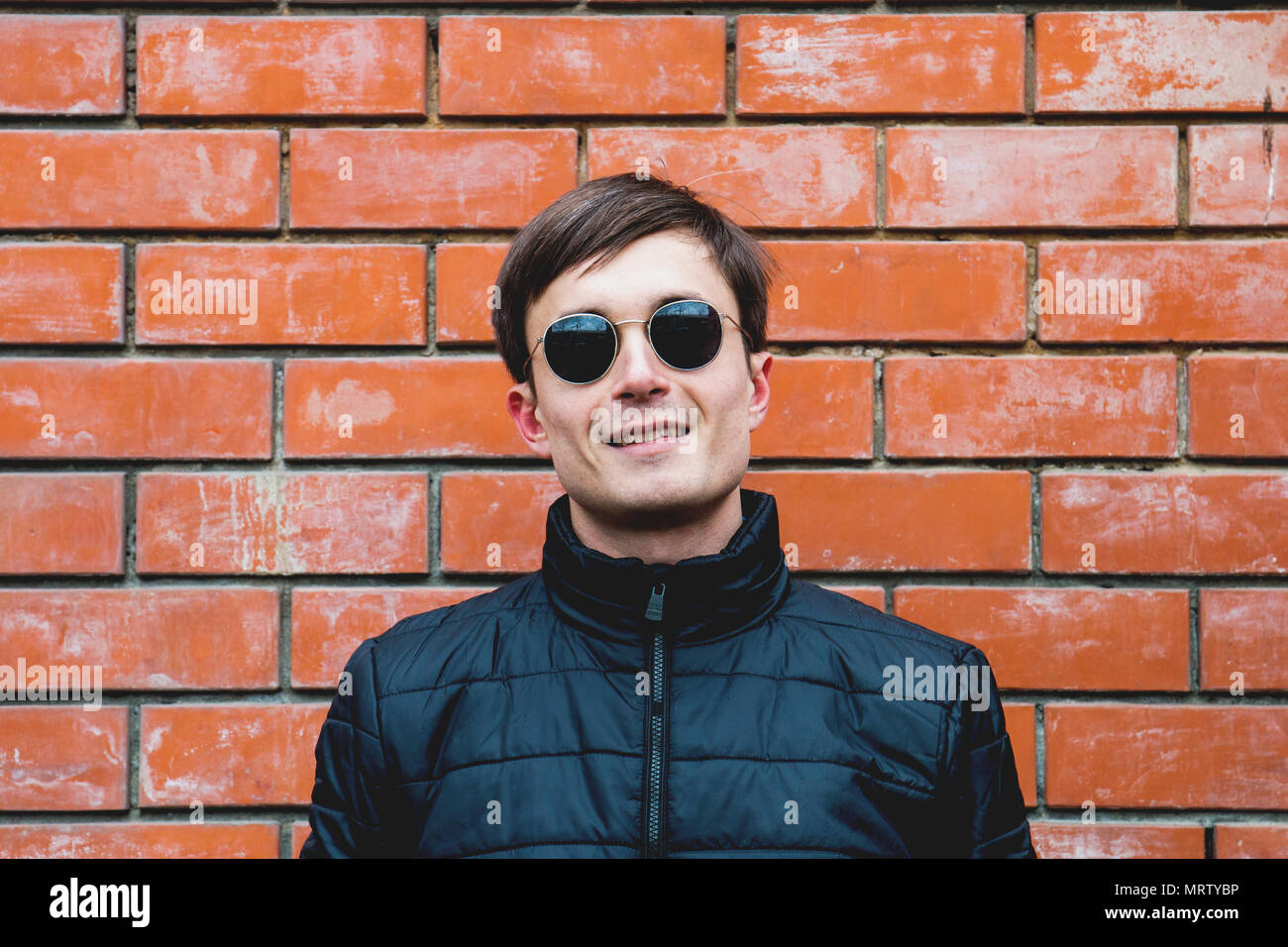 a young man stands leaning against a brick wall in sunglasses Stock ...