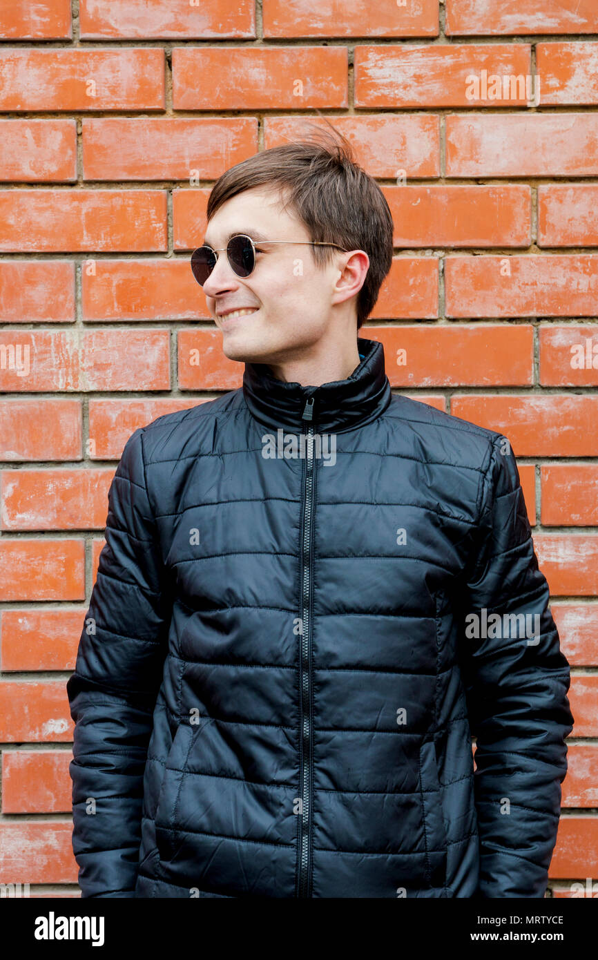 a young man stands leaning against a brick wall and smiling Stock Photo ...