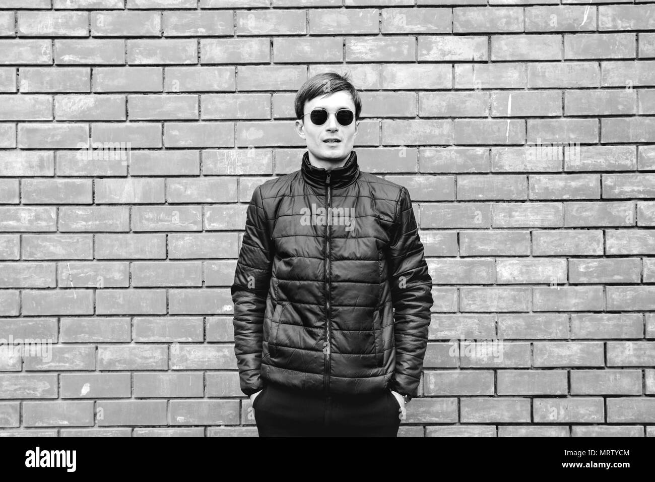 a young man stands leaning against a brick wall in sunglasses black and ...