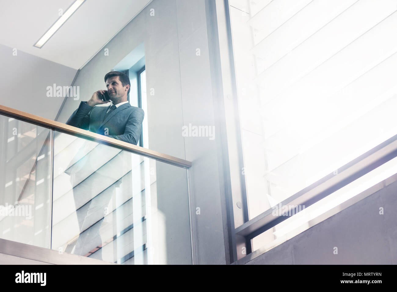 Low angle view businessman standing by railing and talking on mobile phone. Office manager making a phone call in office. Stock Photo
