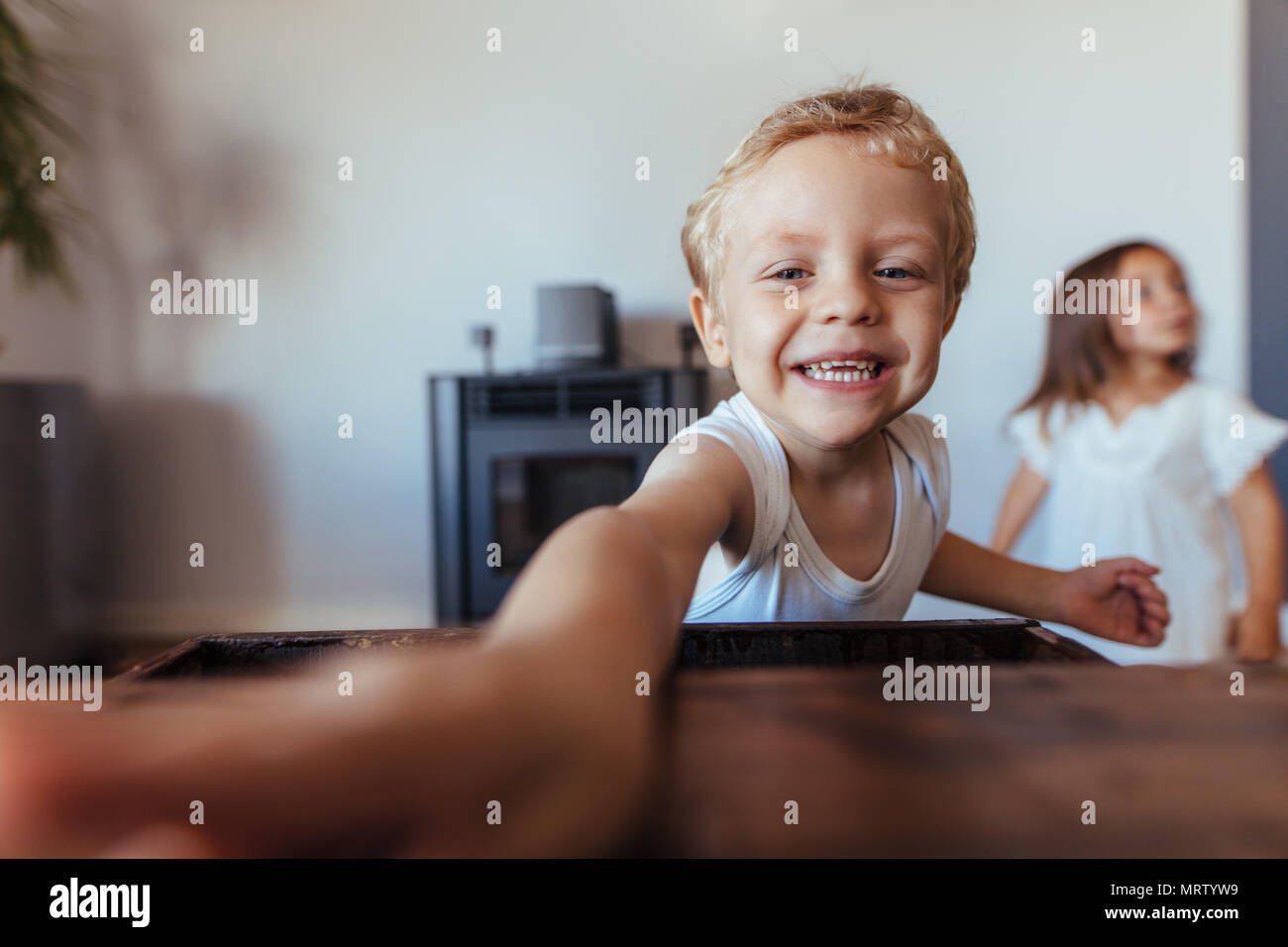 Adorable little boy touching something and smiling with his sister standing at the back. Kids playing at home. Stock Photo