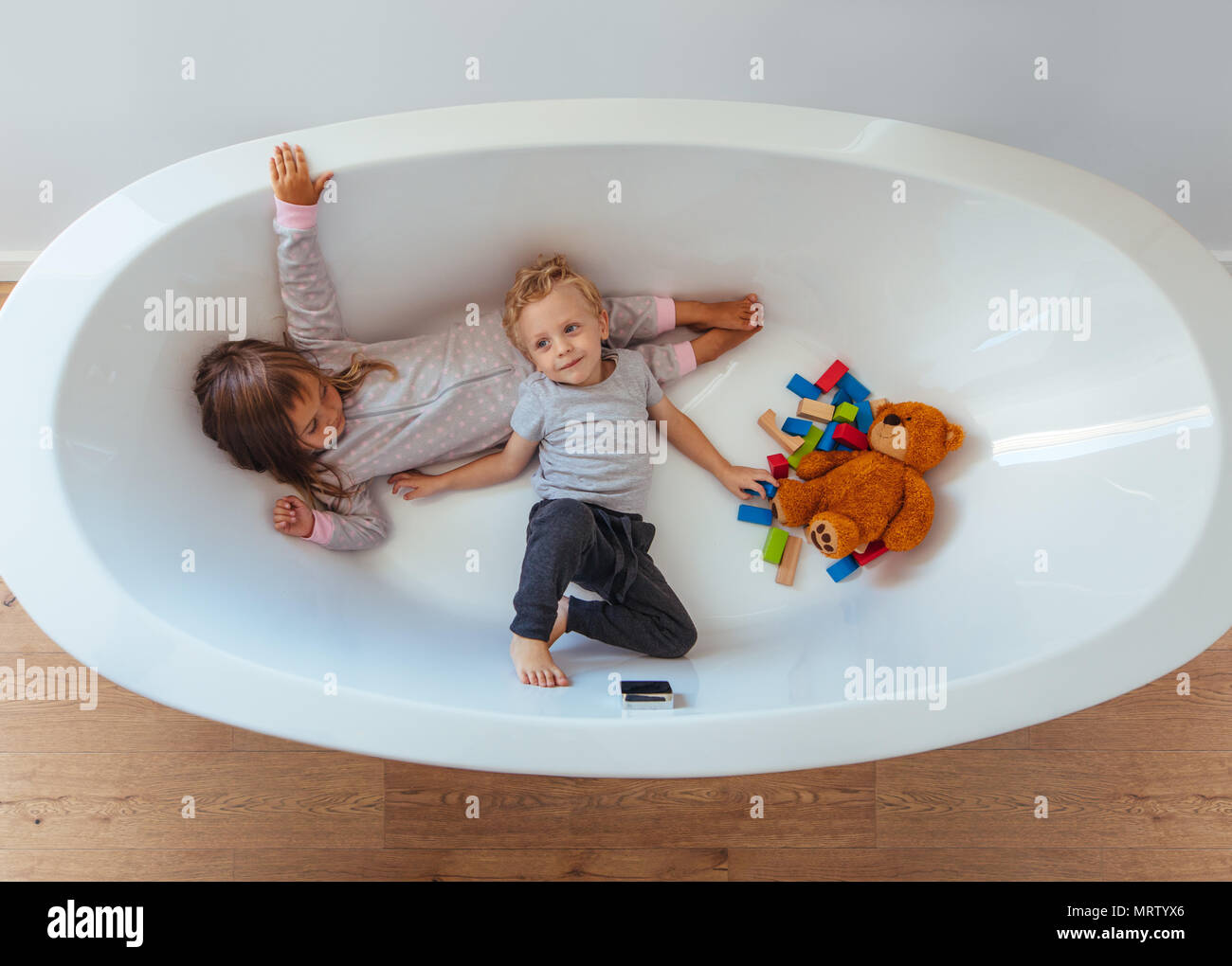 Top view children lying in bathtub with teddy bear and wooden blocks