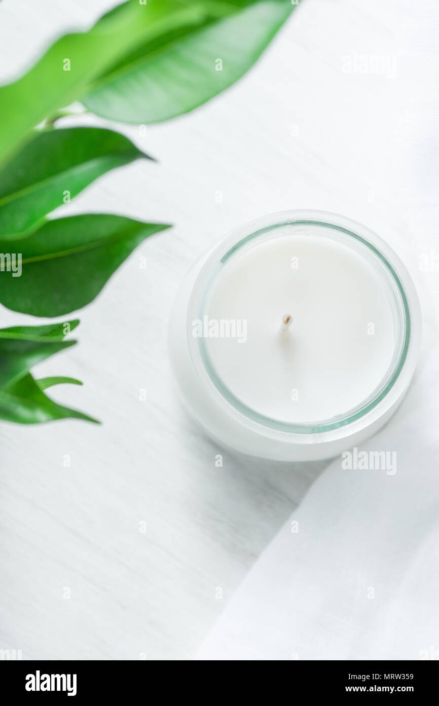 White Candle in Glass Jar Fresh Tree Branches with Tender Green Leaves on Wood and Cotton Linen Fabric Background. Spa Wellness Body Care Meditation C Stock Photo