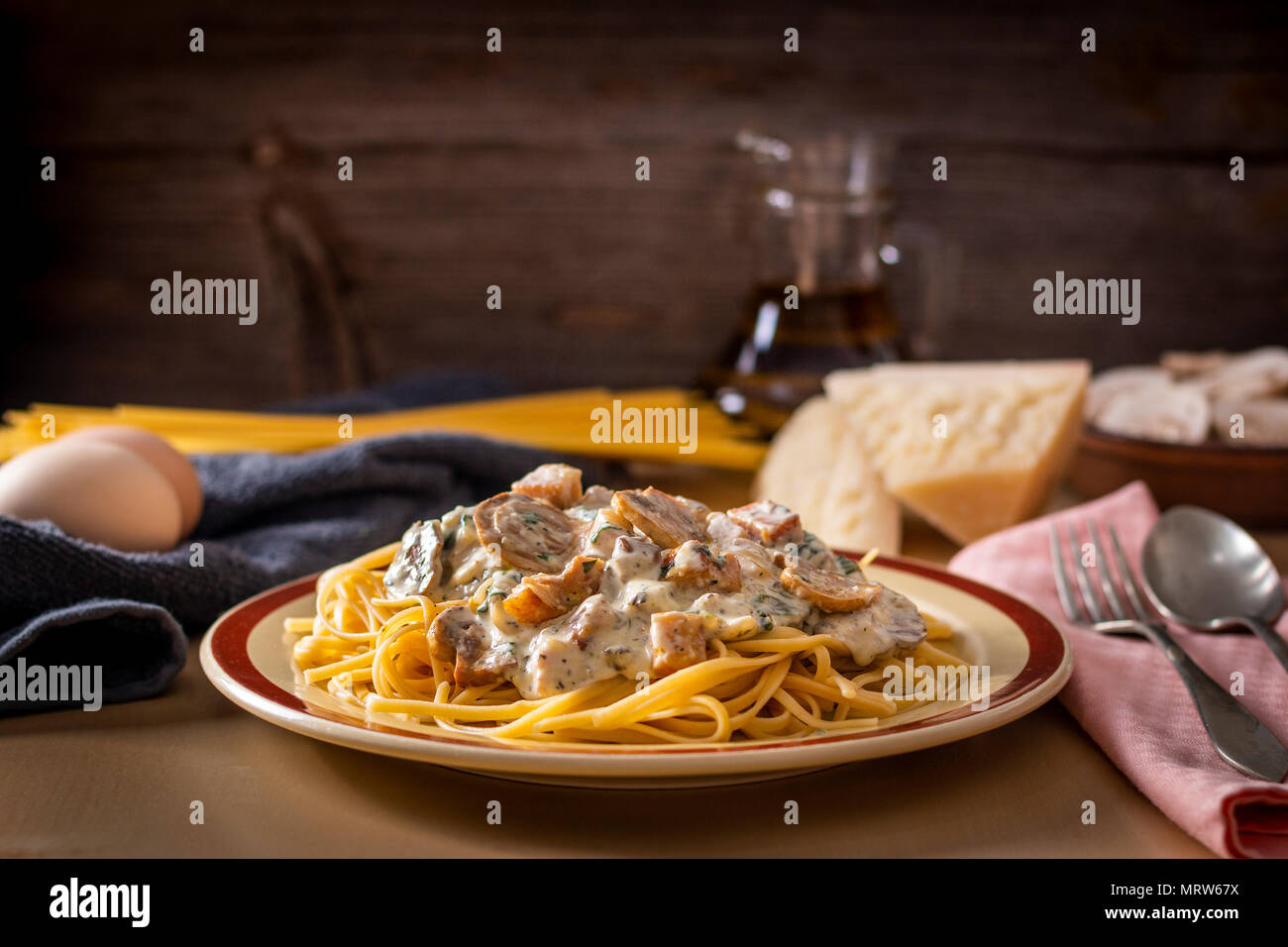 Plate with pasta topped with creamy sauce and mushrooms served on table with cooking ingredients Stock Photo