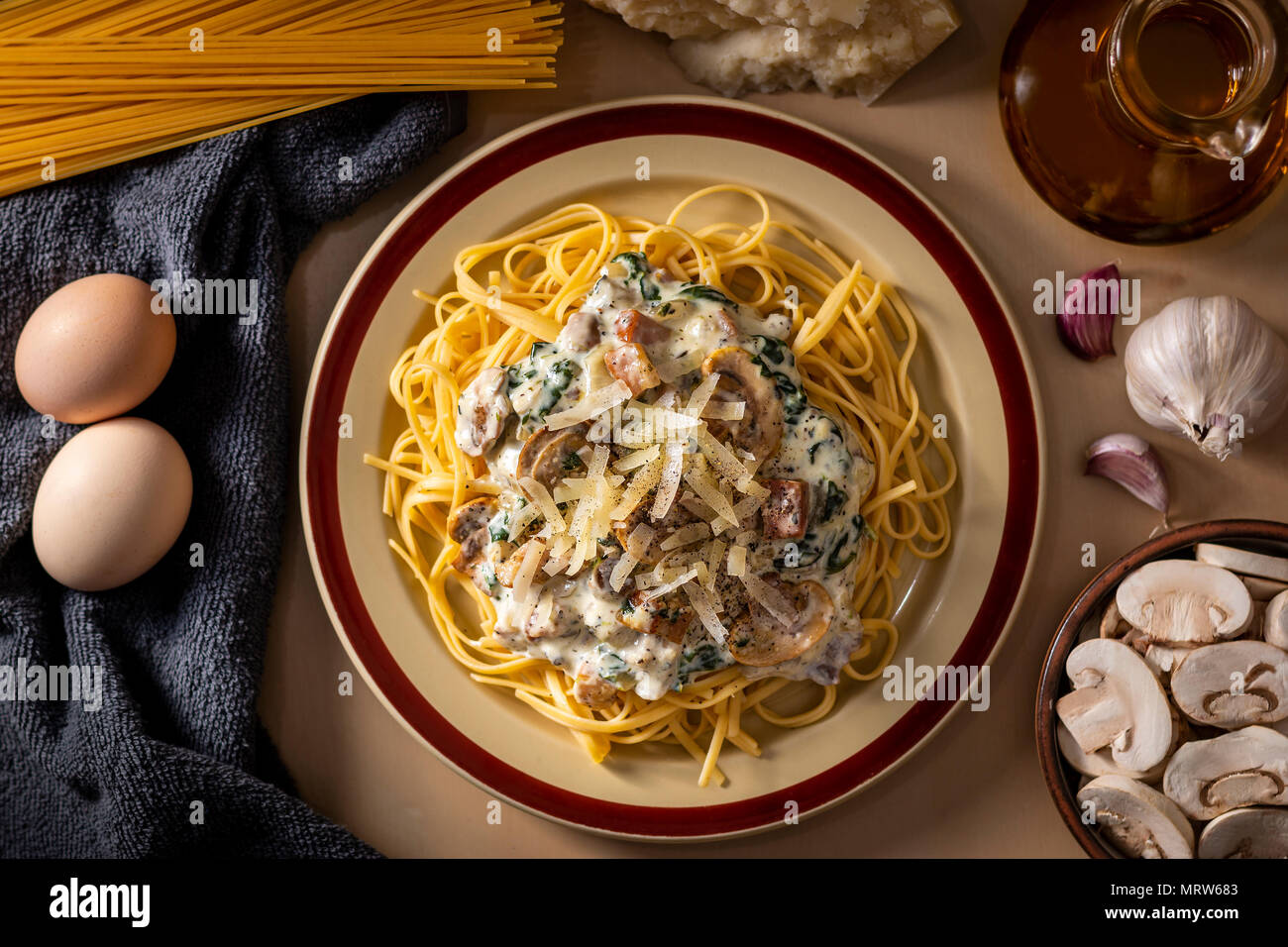 Flat lay of cooked spaghetti with creamy sauce and cheese on top arranged among fresh cooking ingredients Stock Photo