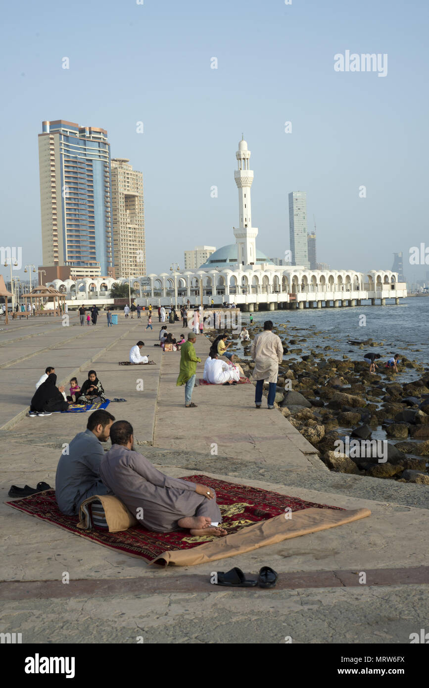 Two men relaxing on a carpet on the Corniche near a famous mosque in Jeddah, Saudi Arabia Stock Photo