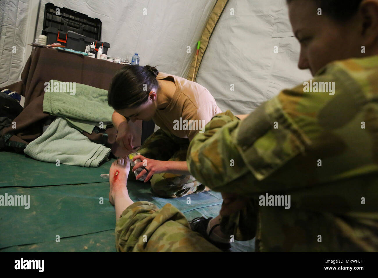 Sergeant Jolene Salter, a  medic with 3rd Health Support Battalion, 17th Combat Service Support Brigade, uses special-effects makeup to create a simulated foot injury on Pvt. Sarah Williams, a medic with 2nd General Health Battalion, 17th CSS Brigade, at Williamson Air Field, Shoalwater Bay Training Area, Queensland, Australia, July 8, 2017 during Talisman Saber 17. Australian Army soldiers with 17th CSS Brigade conducted a mass-casualty exercise at Williamson Air Field hospital to practice Role 2 advanced trauma care and procedures that are used in a deployed environment. Exercises like Talis Stock Photo