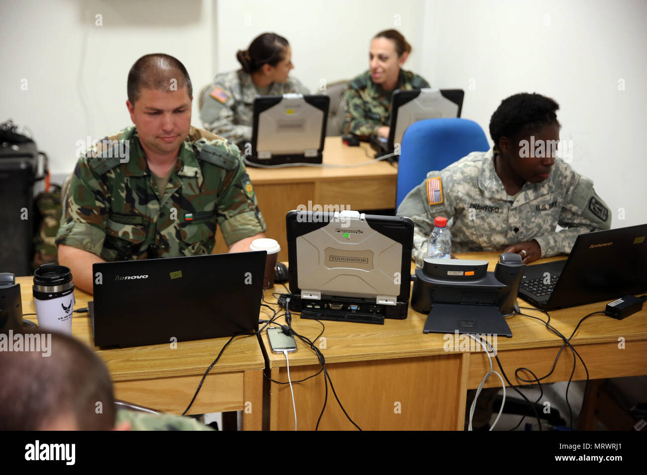 U.S. Army Spc. Cheryl Crawford (front right) and Sgt. Jacline Robledo (back left), both information technology specialists assigned to the 86th Expeditionary Signal Battalion, 11th Signal Brigade, work with Bulgarian Army Soldiers assigned to the 61st Mechanized Brigade G-6 Communications and Information Management section, July 12, 2017 at Novo Selo Training Area, Bulgaria. The 86th Expeditionary Signal Bn. is providing voice and data over Army Coalition Mission Environment, or ACME, network to the 61st Mechanized Brigade to enable a multinational command post exercise as part of exercise Sab Stock Photo