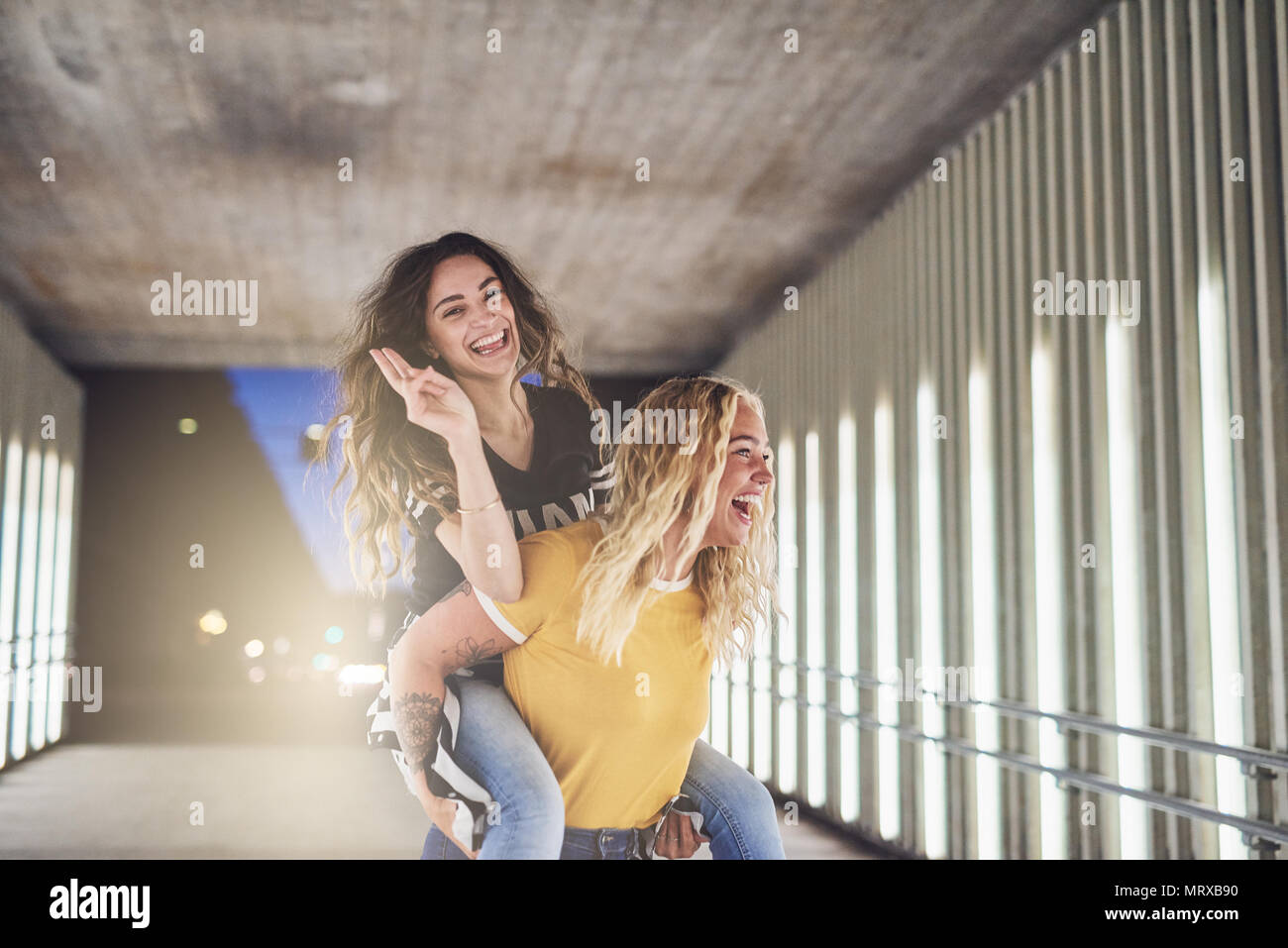 Laughing young woman being carried by her friend while having a fun evening out together in the city Stock Photo