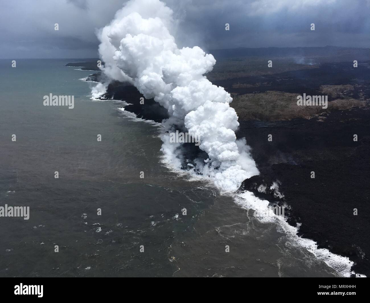 Lava and poisonous sulfur dioxide plumes rise as molten magma reaches the ocean from the eruption of the Kilauea volcano May 26, 2018 in Pahoa, Hawaii. Hot lava entering the ocean creates a dense white plume called 'laze' (short for 'lava haze'). Laze is formed as hot lava boils seawater to dryness. The process leads to a series of chemical reactions that create a billowing white cloud composed of a condensed seawater steam, hydrochloric acid gas, and tiny shards of volcanic glass. The cloud is as corrosive as dilute battery acid, and should be avoided. Stock Photo