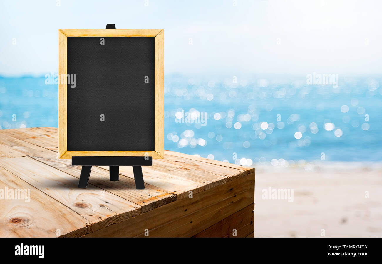 Blank blackboard on wood table food stand with blur sand beach and blue sea with bokeh light background.Template Mock up for summer vacation promotion Stock Photo