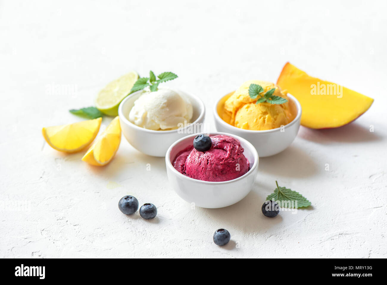 Three various fruit and berries ice creams on white background, copy space. Frozen yogurt or ice cream with lemon, mango, blueberries - healthy summer Stock Photo