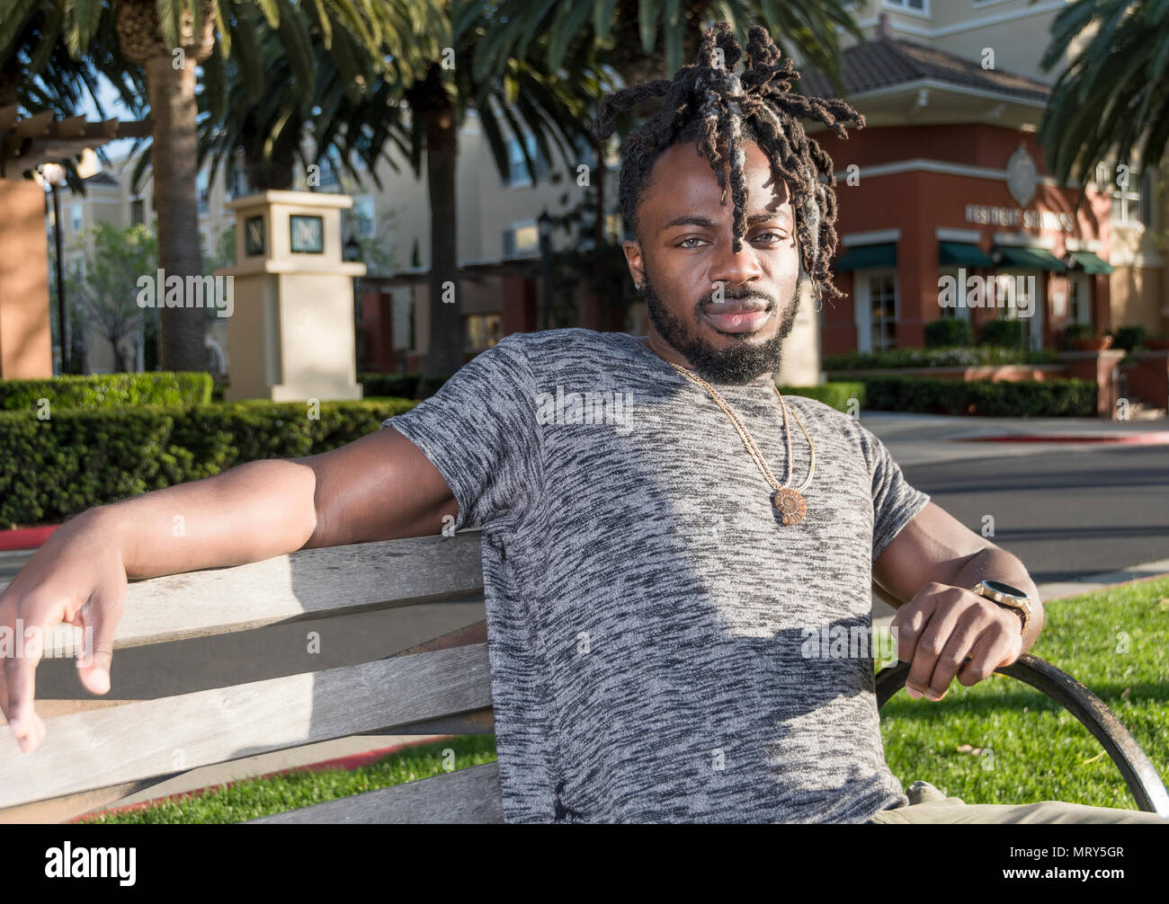 Handsome young African American man sitting on the bench in the park. Stock Photo