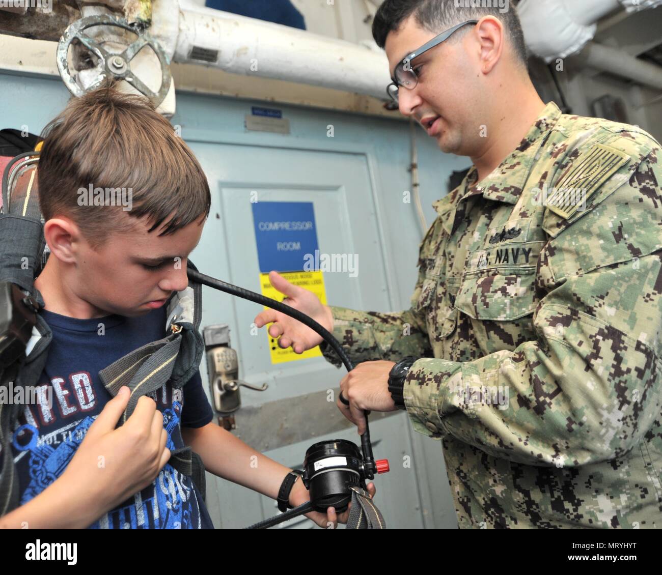 170714-N-YJ133-080 (POLARIS POINT, Guam) July 14, 2017 – Damage Controlman 3rd Class Felipe Zepeda helps a sea cadet from U.S. Naval Sea Cadet Corps Marianas Division Guam don a Self-Contained Breathing Apparatus (SCBA) during a tour of submarine tender USS Emory S. Land (AS 39), July 14. Land and USS Frank Cable (AS 40), the U.S. Navy’s only two submarine tenders, both homeported in Apra Harbor, Guam, provide maintenance, hotel services and logistical support to submarines and surface ships in the U.S. 5th and 7th Fleet areas of operation. (U.S. Navy photo by Mass Communication Specialist 2nd Stock Photo