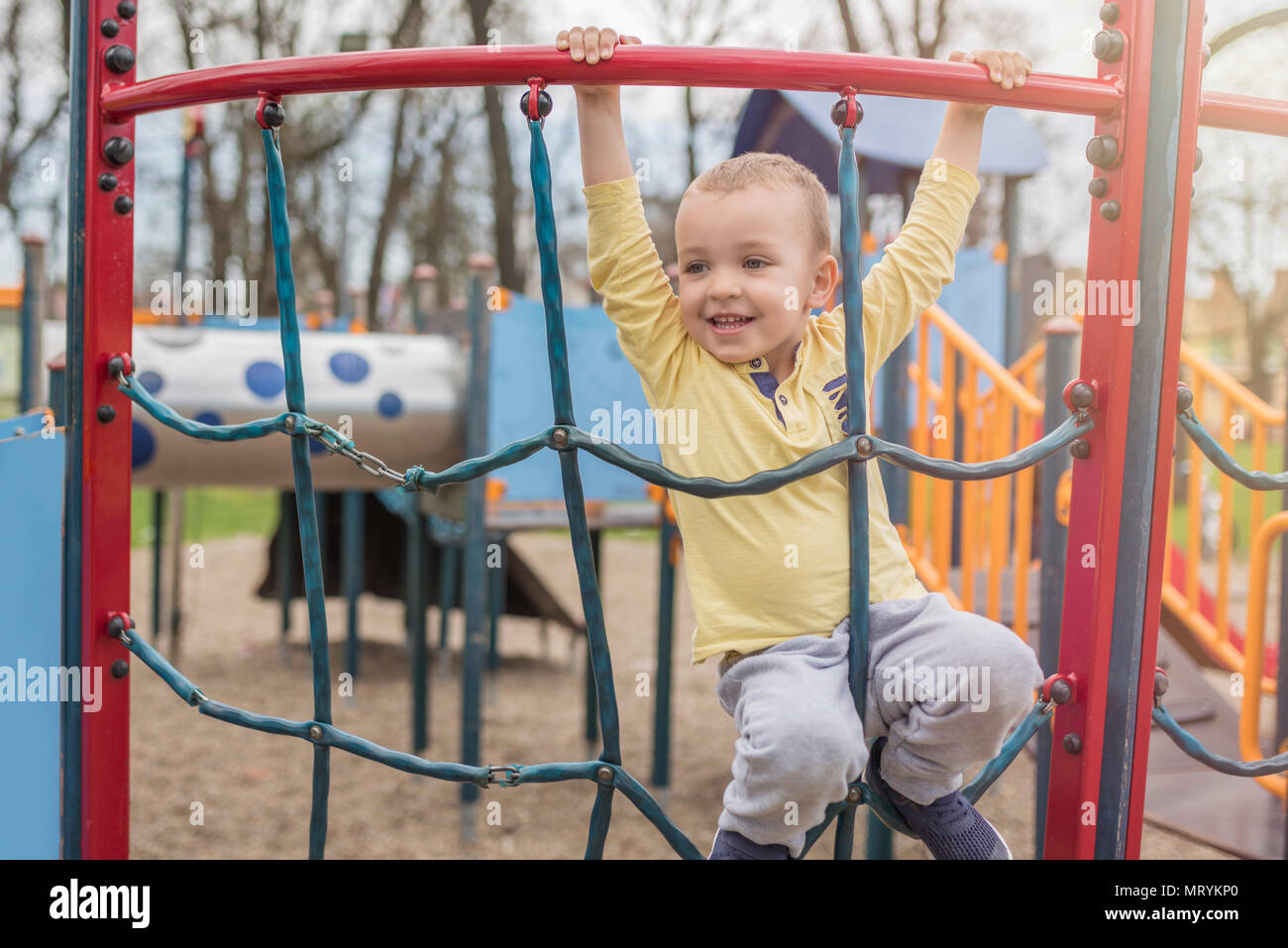 Adorable little boy having fun on playground. Active sport leisure for kids in park. Little boy with blue eyes in yellow shirt playing on playground. Stock Photo