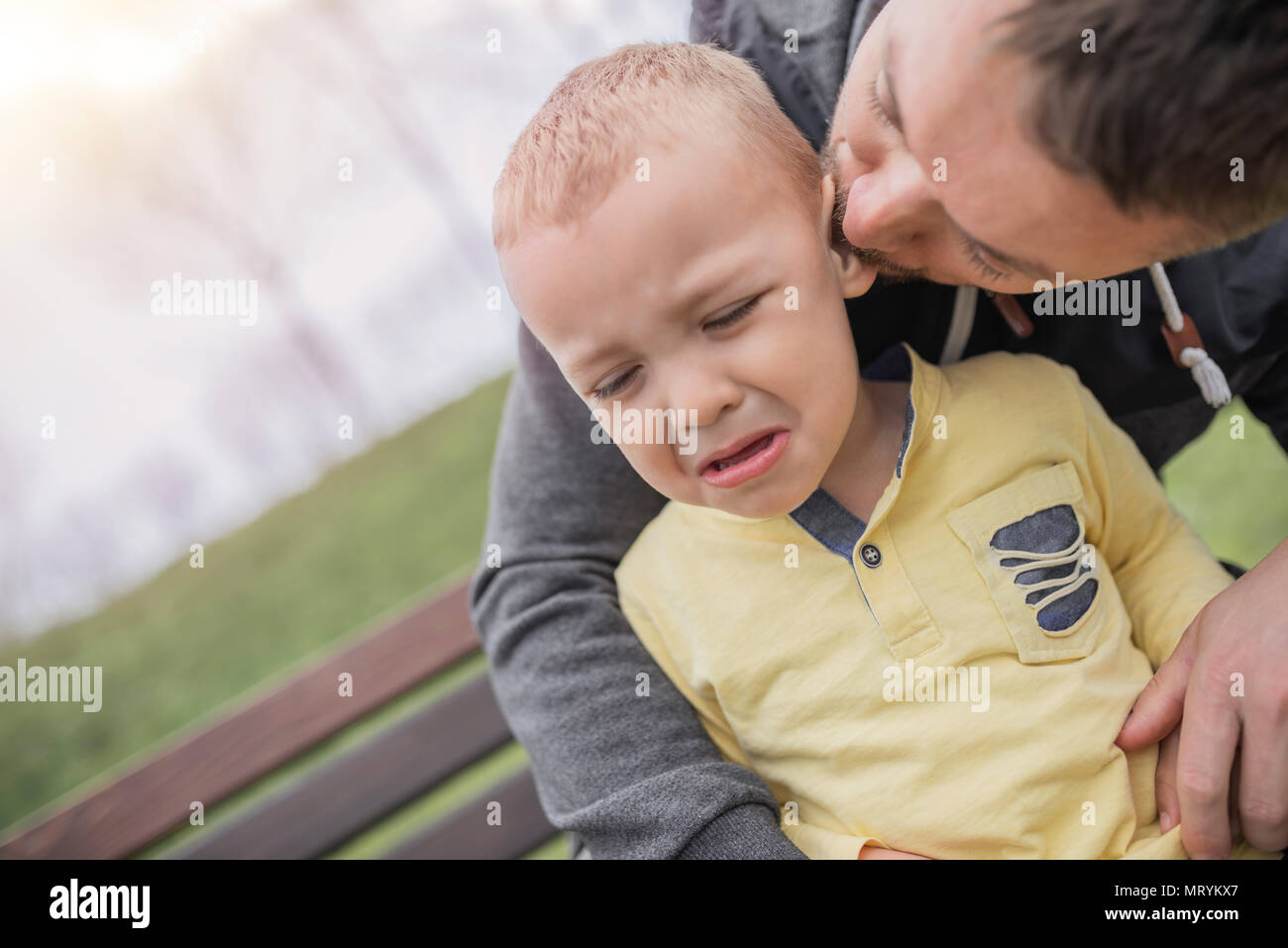 Closeup portrait of a young father and crying kid on playground. Young father hugs crying child. Dad and son. Stock Photo