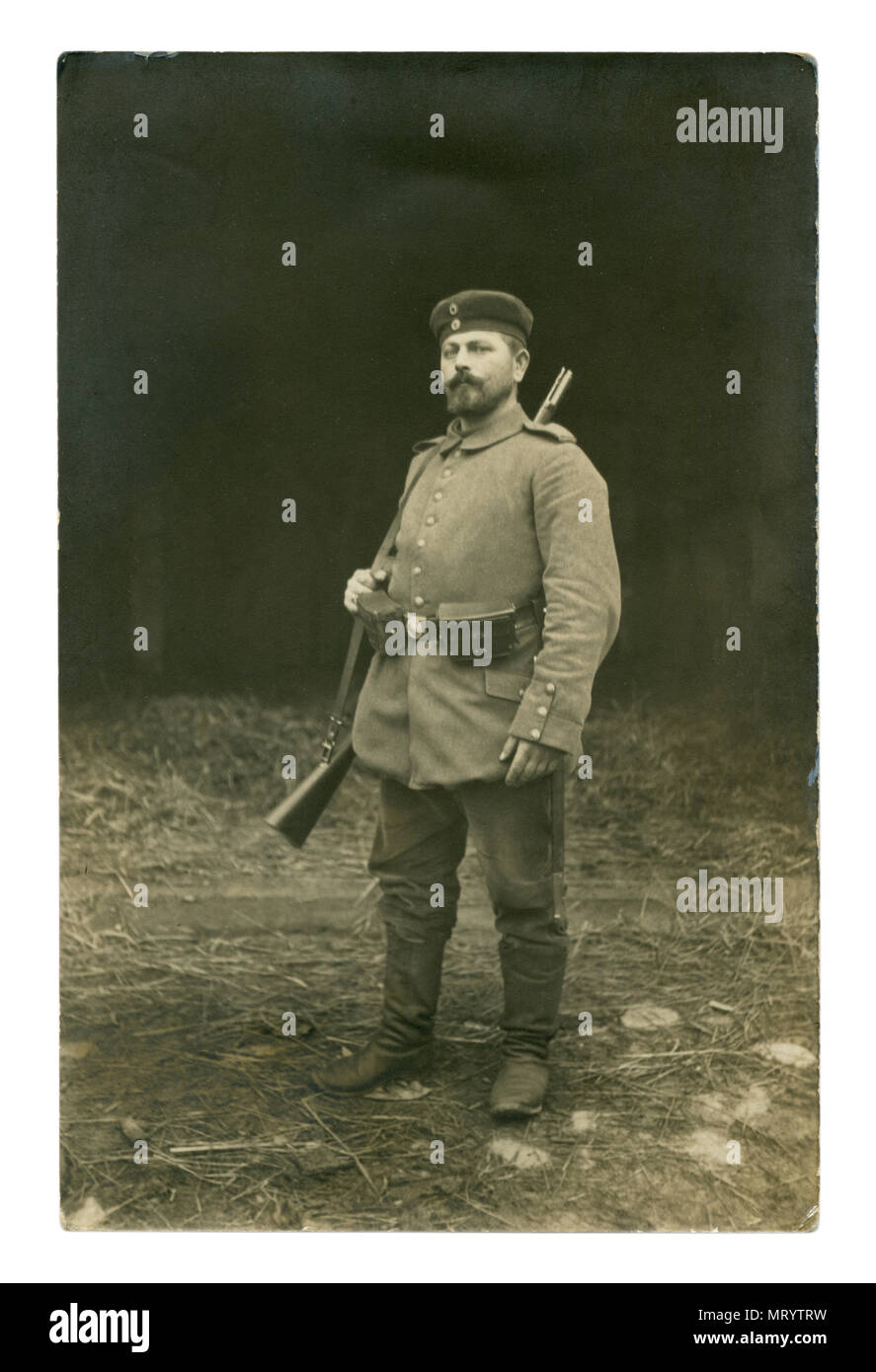 German historical photo: a soldier with a beer belly in military uniform in full gear with a rifle over his shoulder posing outside. world war one Stock Photo