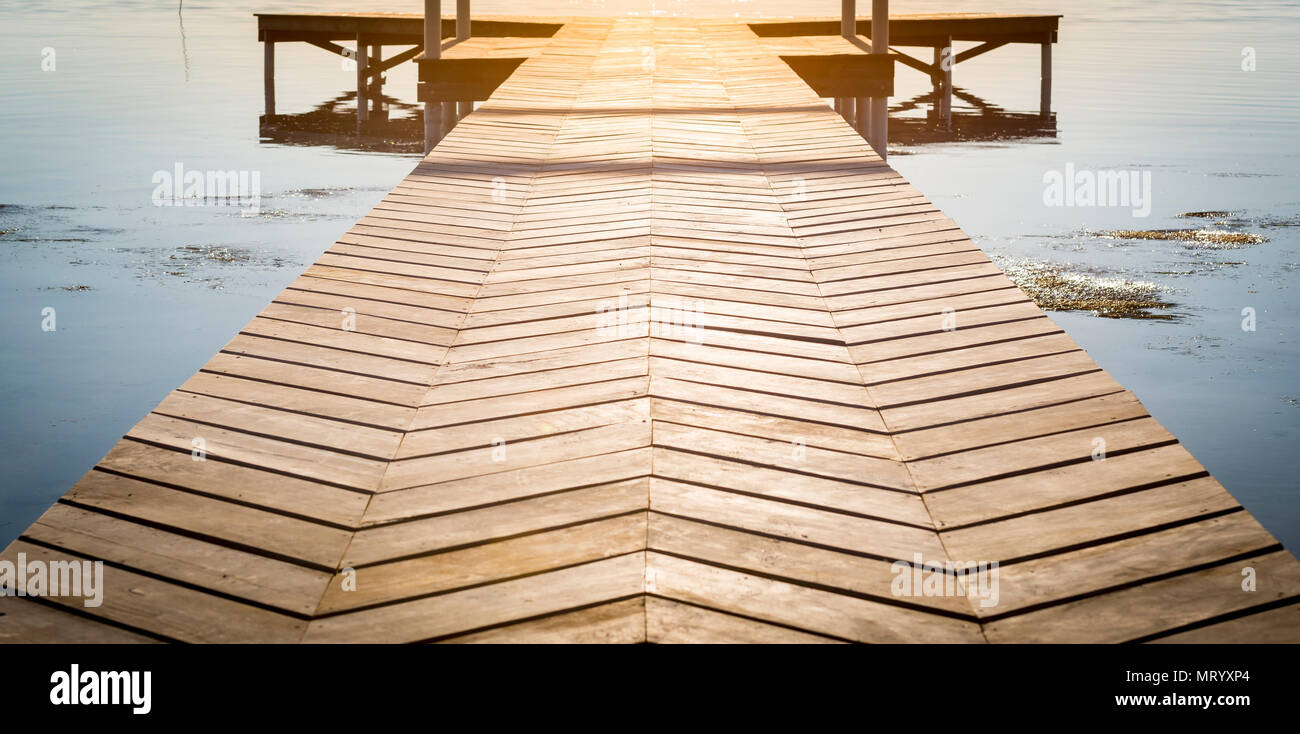 Background of wooden dock over calm water at sunrise with copy space Stock Photo