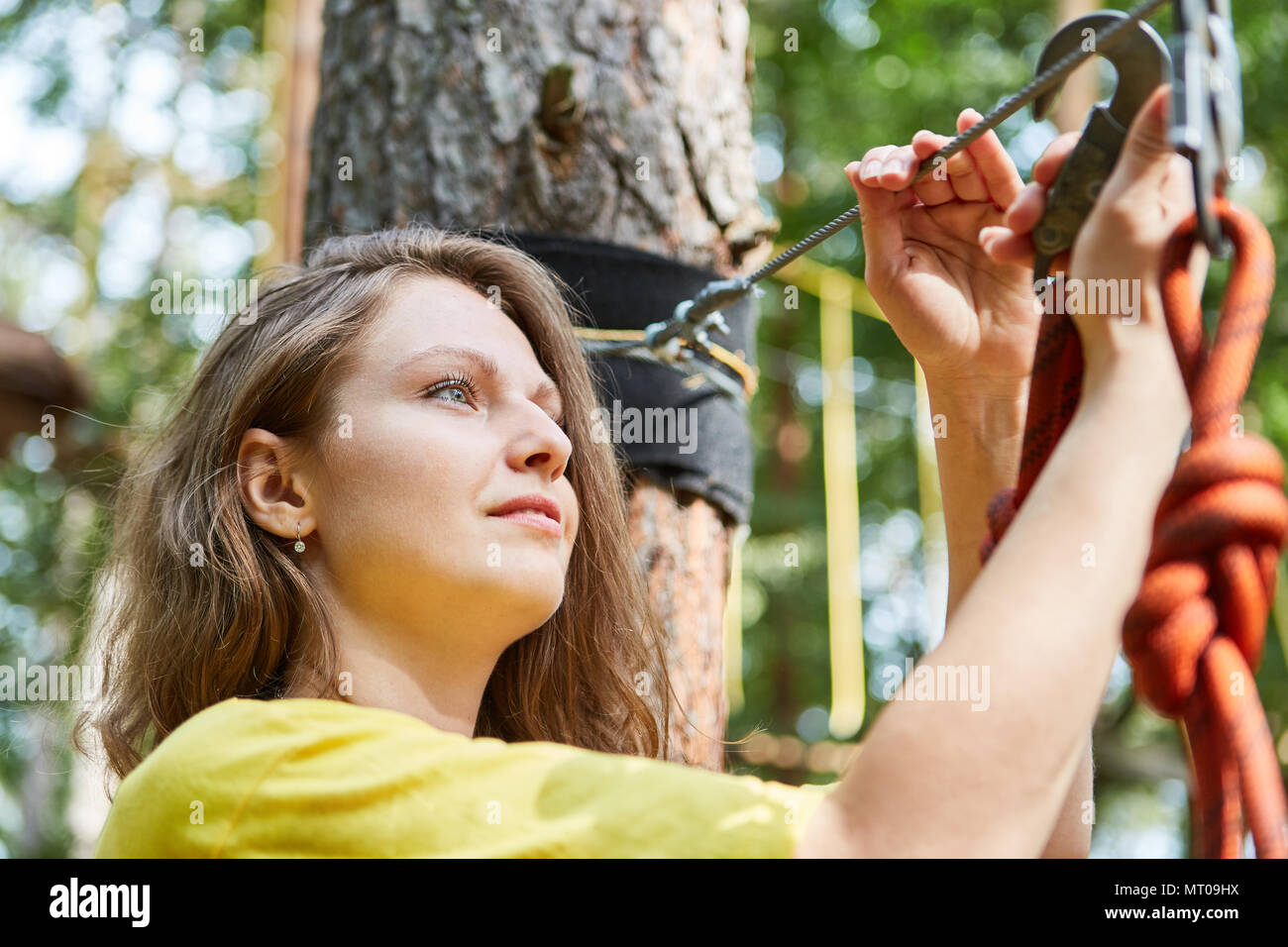 Young woman in tightrope garden at startup fastens her snap hook to the rope Stock Photo