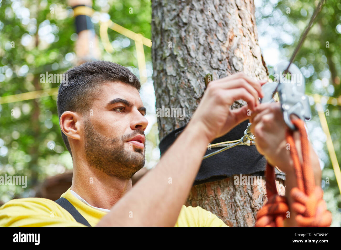 Young man in climbing forest carefully inspects rope and snap hook