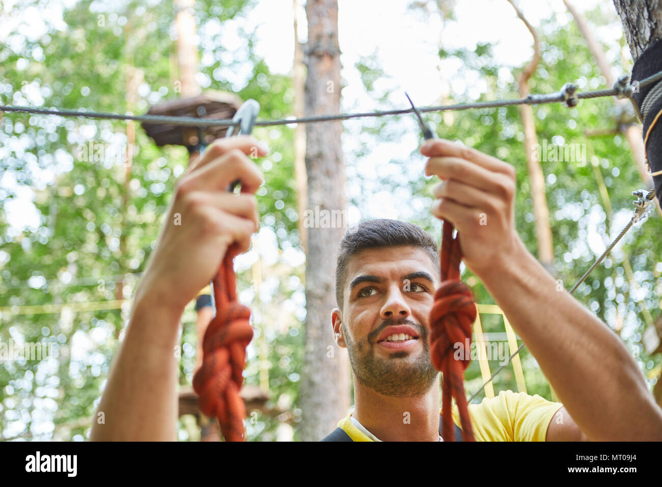 Young man in climbing forest fastens a carbine at the teambuilding workshop Stock Photo