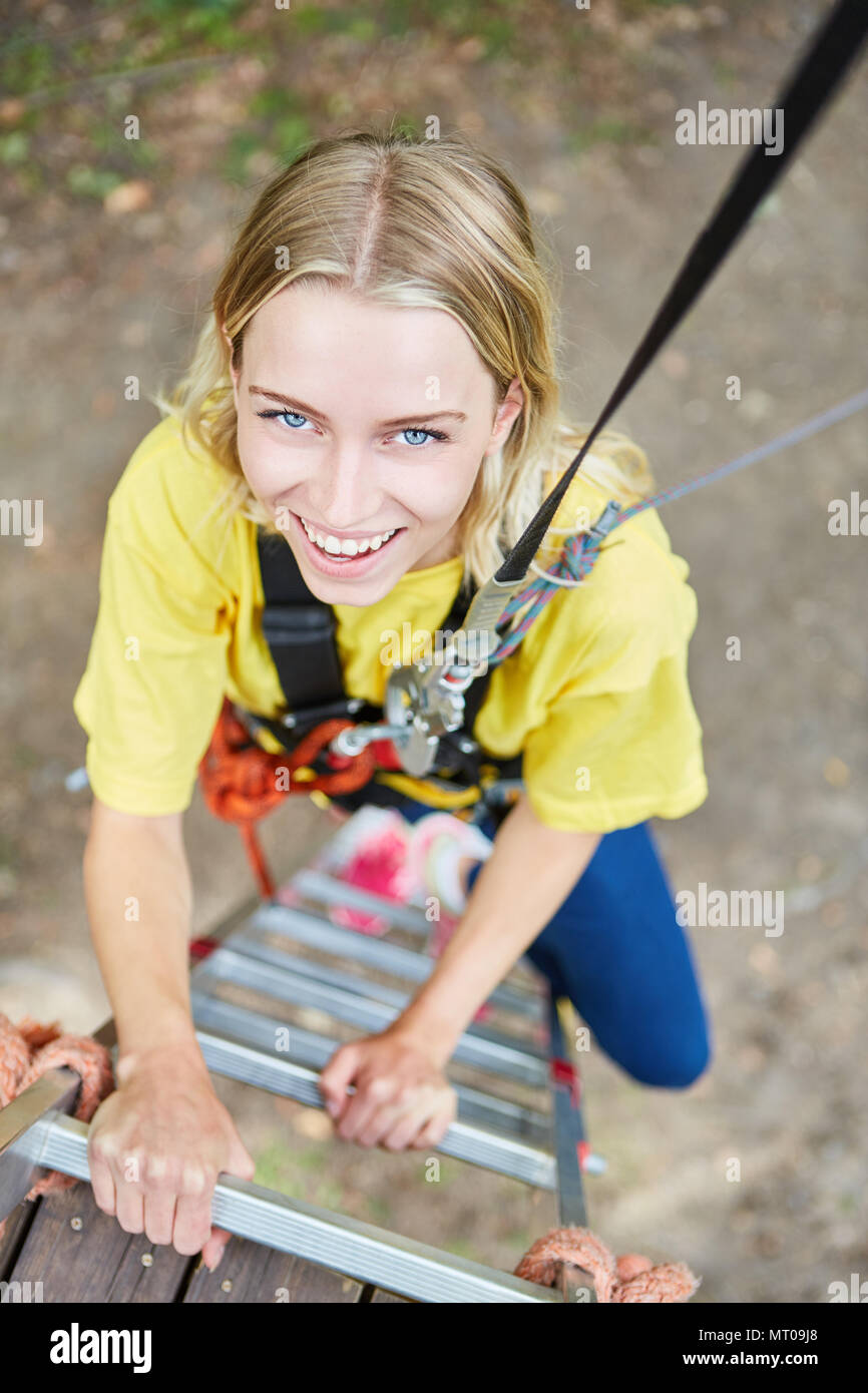 Young woman climbs up a ladder in high wire garden in teambuilding workshop Stock Photo