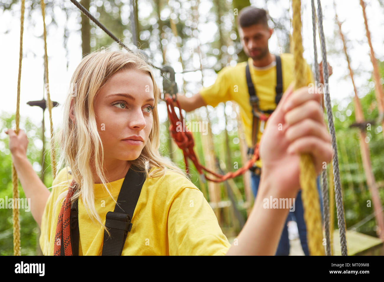 Fearful young woman struggles with vertigo on a bridge in the high ropes course Stock Photo