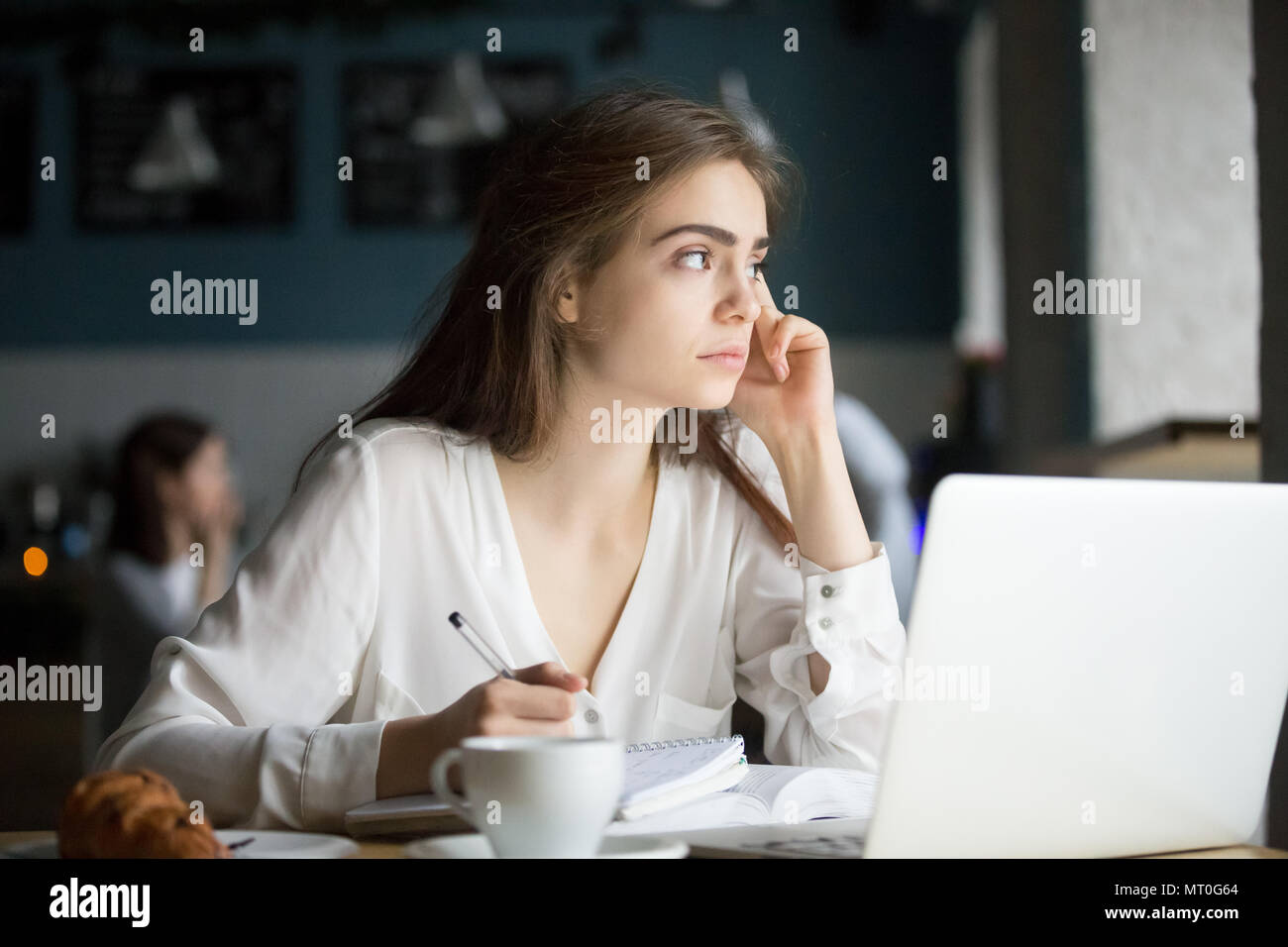 Thoughtful female writer or student writing notes in coffee shop Stock Photo