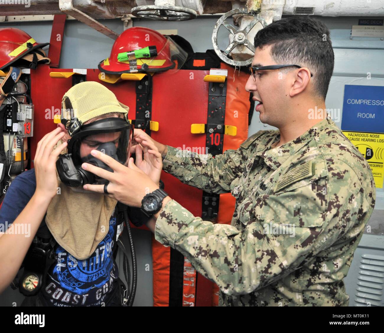170714-N-YJ133-095 (POLARIS POINT, Guam) July 14, 2017 – Damage Controlman 3rd Class Felipe Zepeda helps a sea cadet from U.S. Naval Sea Cadet Corps Marianas Division Guam don flash gear during a tour of submarine tender USS Emory S. Land (AS 39), July 14. Land and USS Frank Cable (AS 40), the U.S. Navy’s only two submarine tenders, both homeported in Apra Harbor, Guam, provide maintenance, hotel services and logistical support to submarines and surface ships in the U.S. 5th and 7th Fleet areas of operation. (U.S. Navy photo by Mass Communication Specialist 2nd Class Richard A. Miller/RELEASED Stock Photo