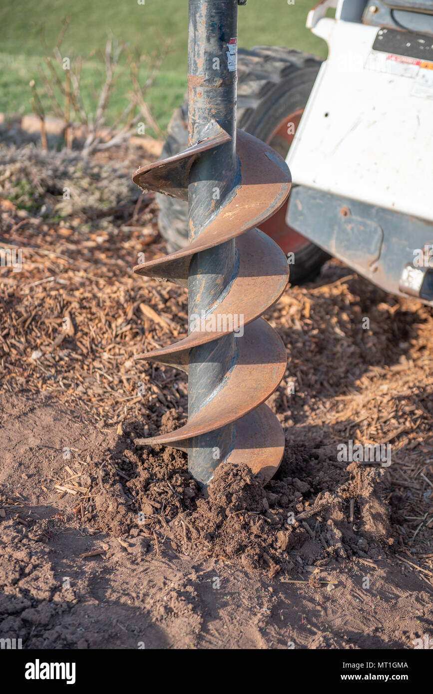 A hydraulic power auger controlled from a skid steer drills a hole in the ground for a cement pad Stock Photo