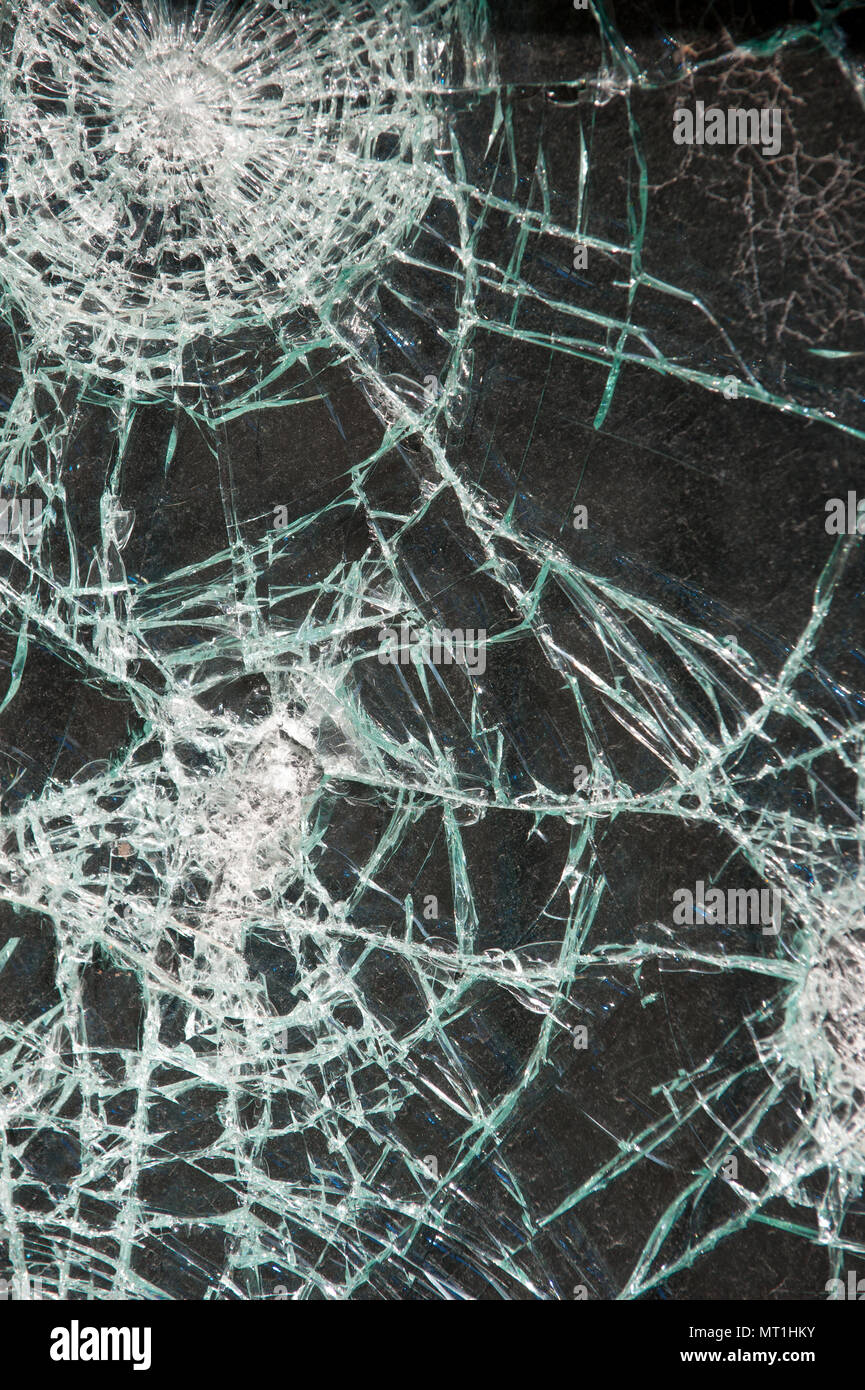 Close-up of a shattered glass window with multiple impact points and spiderweb cracks, highlighting vandalism or accidental damage to property Stock Photo