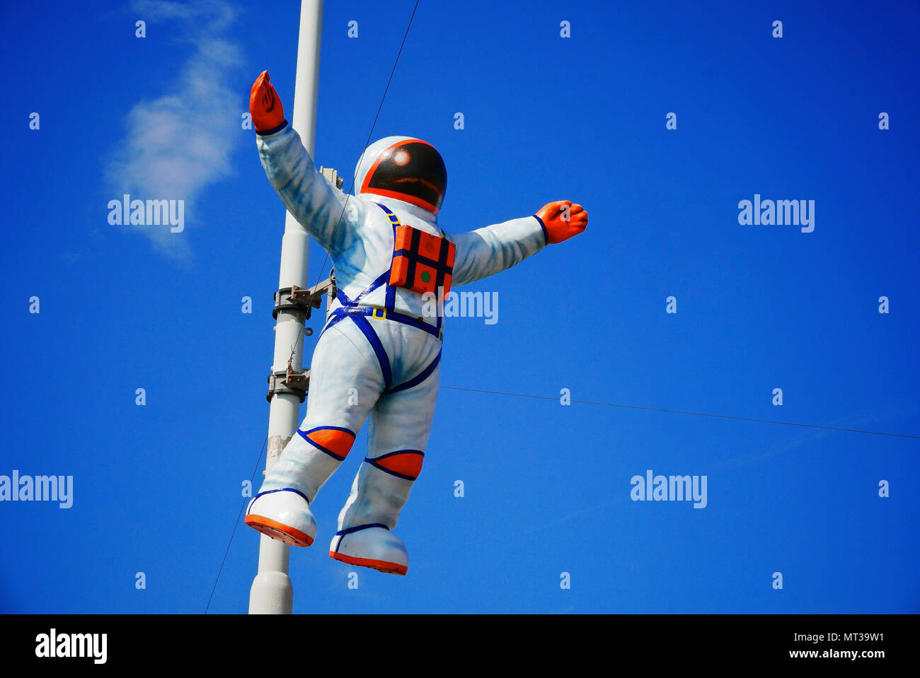 Astronaut in space suit attached to lamp post set against blue sky Stock Photo