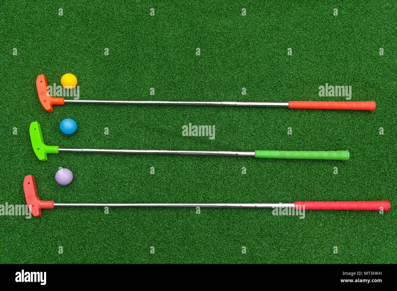 Three horizontal mini golf putters with three mini golf balls on artificial grass Stock Photo