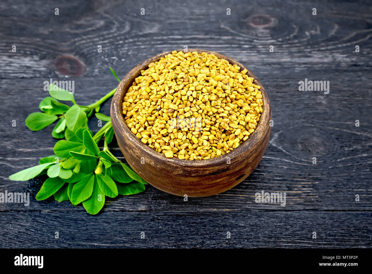 Fenugreek seeds in a clay bowl with green leaves against a black wooden board Stock Photo