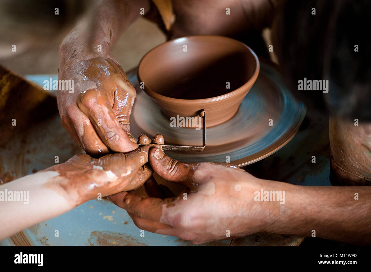 Potter's hands guiding child's hands to help him to work with the pottery wheel Stock Photo