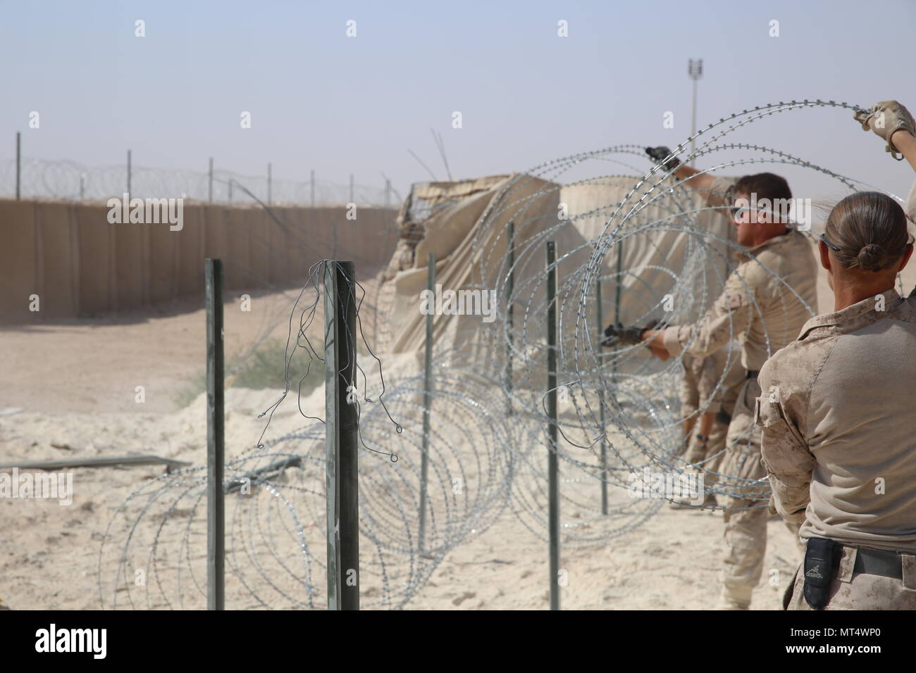 U.S. Marine Corps Cpl. Bridget Bastian and Lance Cpl. Jonathan Fer, both combat engineers attached to Task Force Al Asad with Marine Wing Support Squadron (MWSS) 372 ,Special Purpose Marine Air-Ground Task Force-Crisis Response-Central Command, improve force protection measures by laying concertina wire at Al Asad Air Base, Iraq, July 6, 2017. The Marines of the Engineering Detachment work daily on a variety of engineer tasks in support of the master base plan for Task Force Al Asad. Task Force Al Asad’s mission is to advise and assist  and build partner capacity with the Iraqi Security Forces Stock Photo