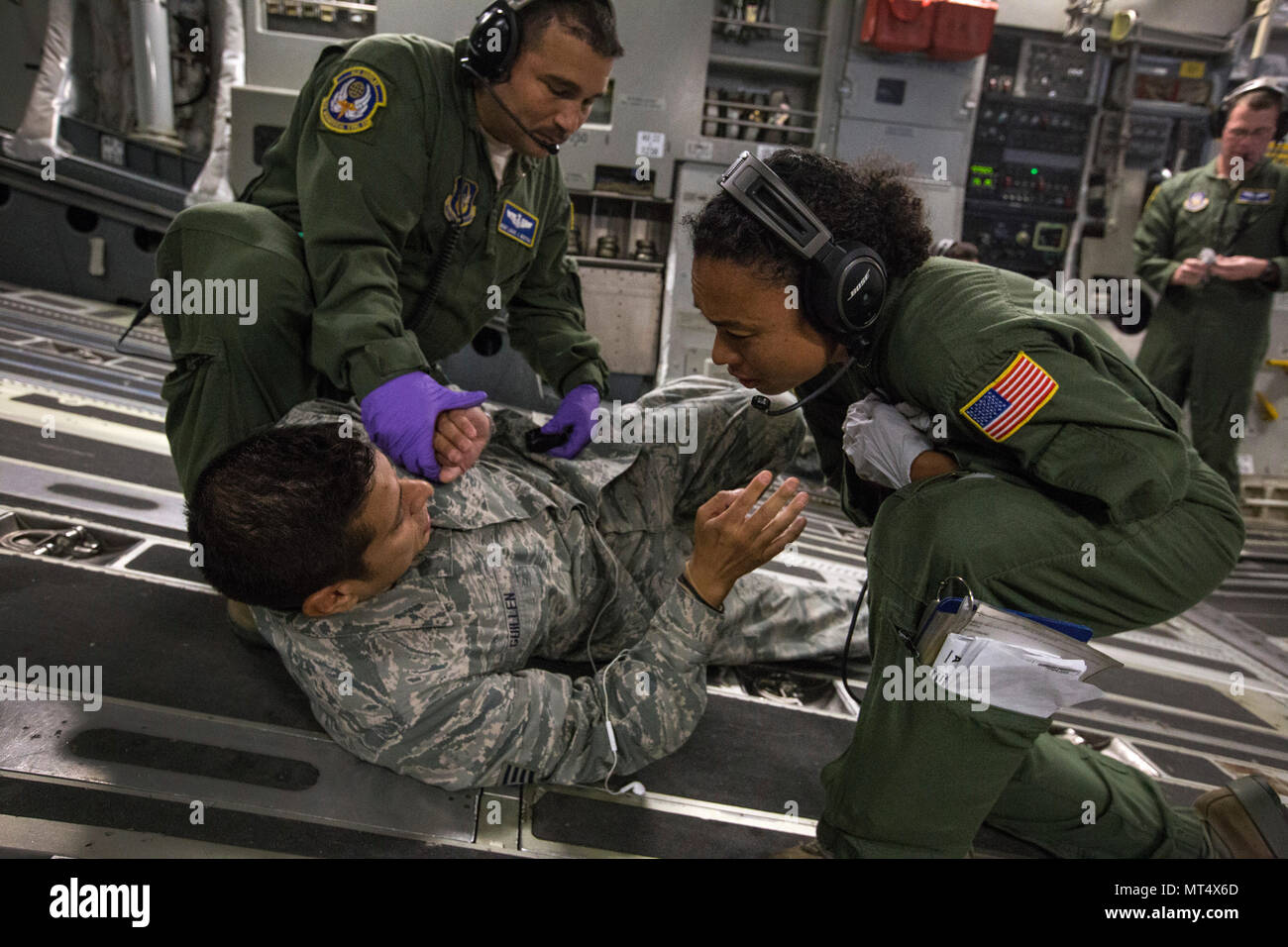 U.S. Air Force Master Sgt. Linda W. Daniels, right, and Master Sgt. Louis J. Muzyka, left, both aeromedical evacuation technicians, assist simulated psychiatric outpatient Staff Sgt. Edward Guillen, all with the 514th Aeromedical Evacuation Squadron, 514th Air Mobility Wing, during an aeromedical evacuation training mission onboard a 305th Air Mobility Wing C-17 Globemaster III to Nashville, Tenn., July 29, 2017. The training’s purpose is to teach flight nurses and aeromedical evacuation technicians how to respond to scenarios during the evacuation of sick or wounded personnel, and how to hand Stock Photo