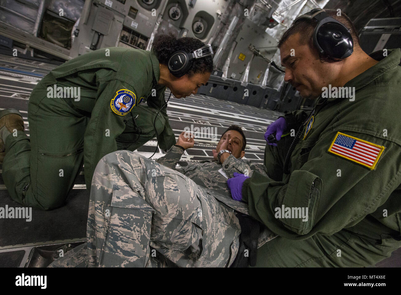 U.S. Air Force Master Sgt. Linda W. Daniels, left, and Master Sgt. Louis J. Muzyka, right, both aeromedical evacuation technicians, assist simulated psychiatric outpatient Staff Sgt. Edward Guillen, all with the 514th Aeromedical Evacuation Squadron, 514th Air Mobility Wing, during an aeromedical evacuation training mission onboard a 305th Air Mobility Wing C-17 Globemaster III to Nashville, Tenn., July 29, 2017. The training’s purpose is to teach flight nurses and aeromedical evacuation technicians how to respond to scenarios during the evacuation of sick or wounded personnel, and how to hand Stock Photo