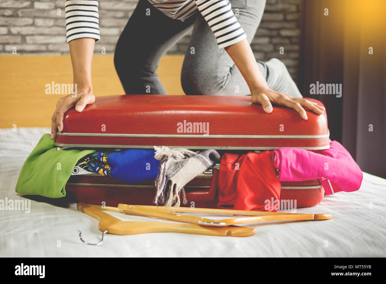 Woman trying to fit all clothing to packing her red suitcase before