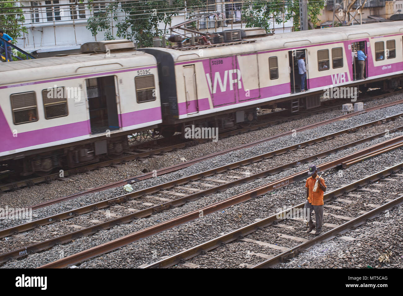 Railway worker walking on the tracks of the local train in Mumbai as a  train passes him by. Stock Photo