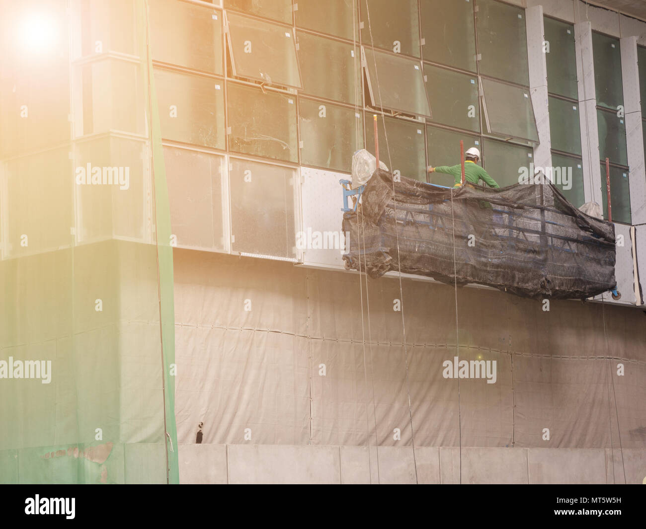 workers in suspended platform working to cutting steel out of new building. Stock Photo