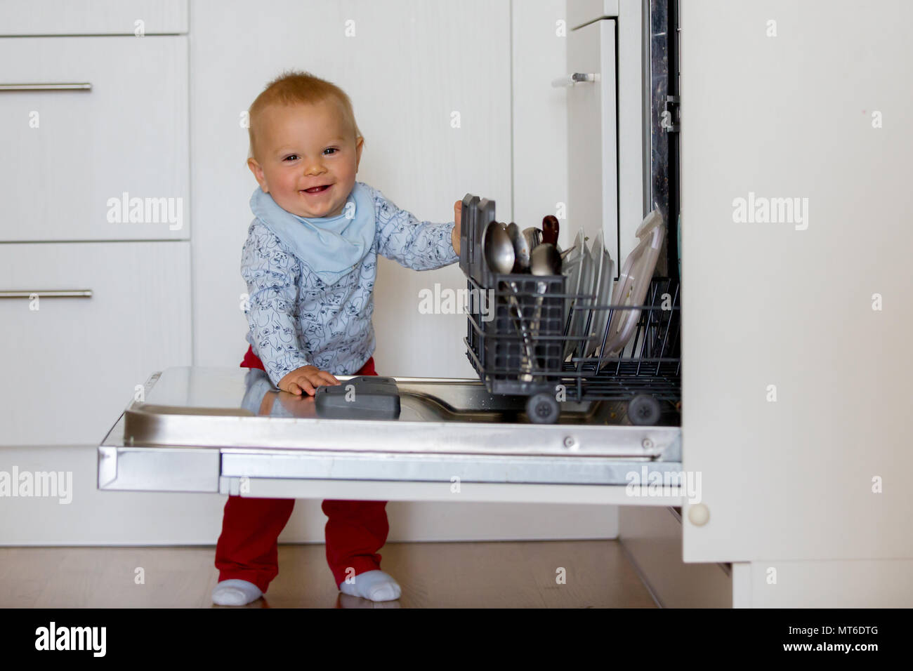 Toddler child, boy, helping mom, putting dirty dishes in dishwasher at home, modern kitchen Stock Photo