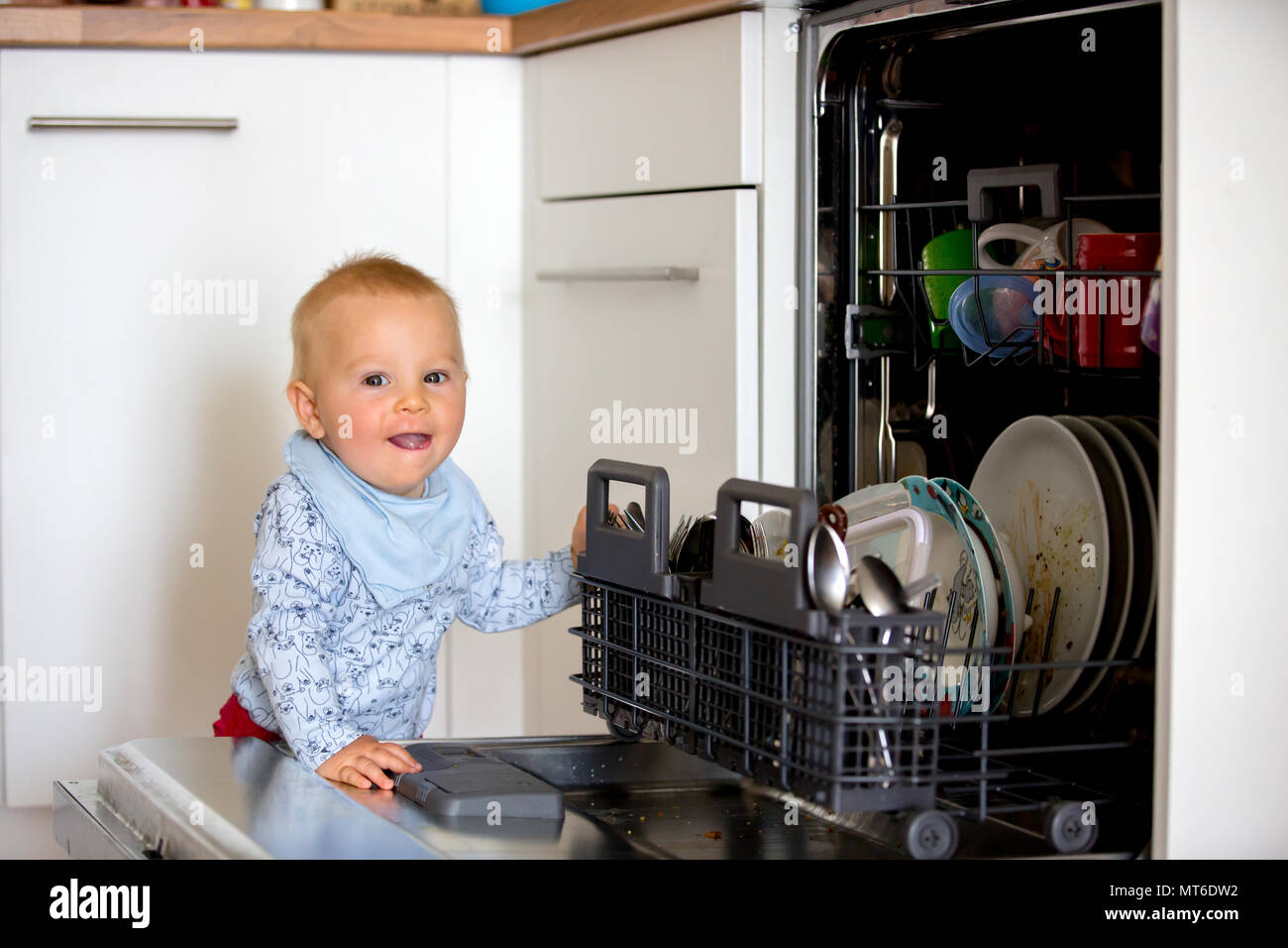 Toddler child, boy, helping mom, putting dirty dishes in dishwasher at home, modern kitchen Stock Photo