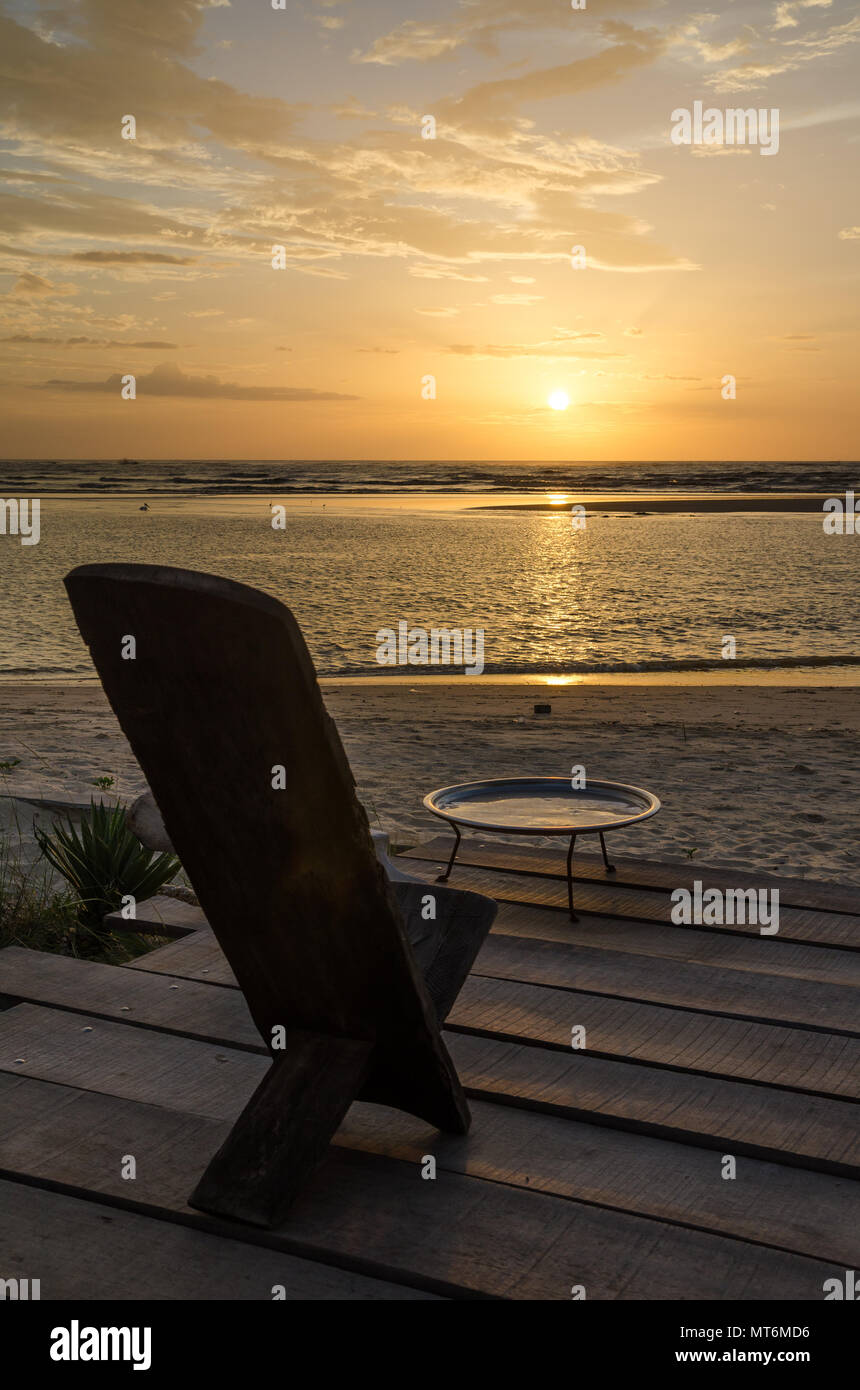 Traditional wooden African chair on terrasse at beach overlooking the ocean during beautiful sunset, Senegal, Africa Stock Photo