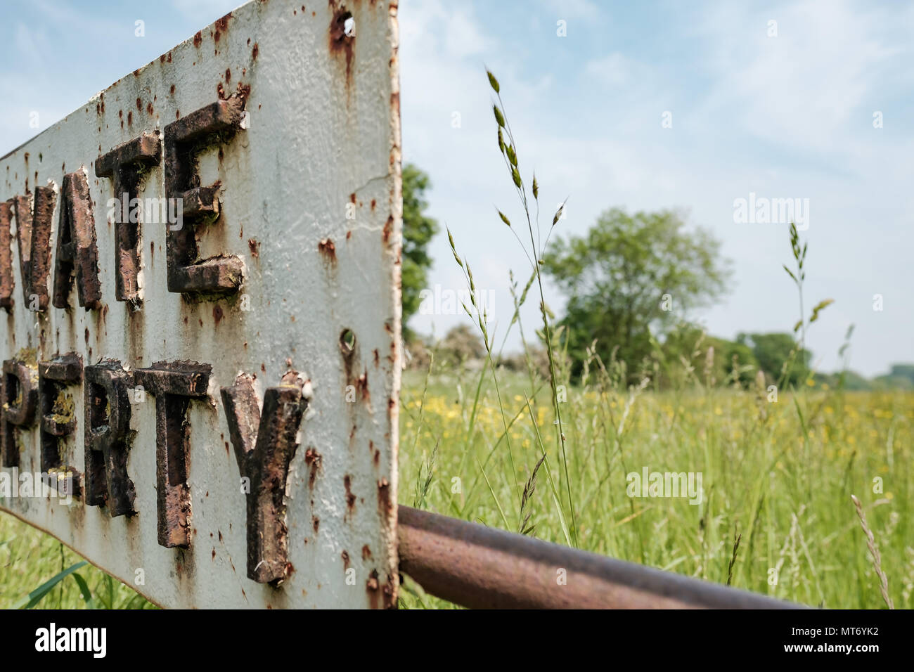 Close-up, abstract image of part of a metal Private Property sign attached to a locked farm gate. Meadow grass can be seen in the background. Stock Photo