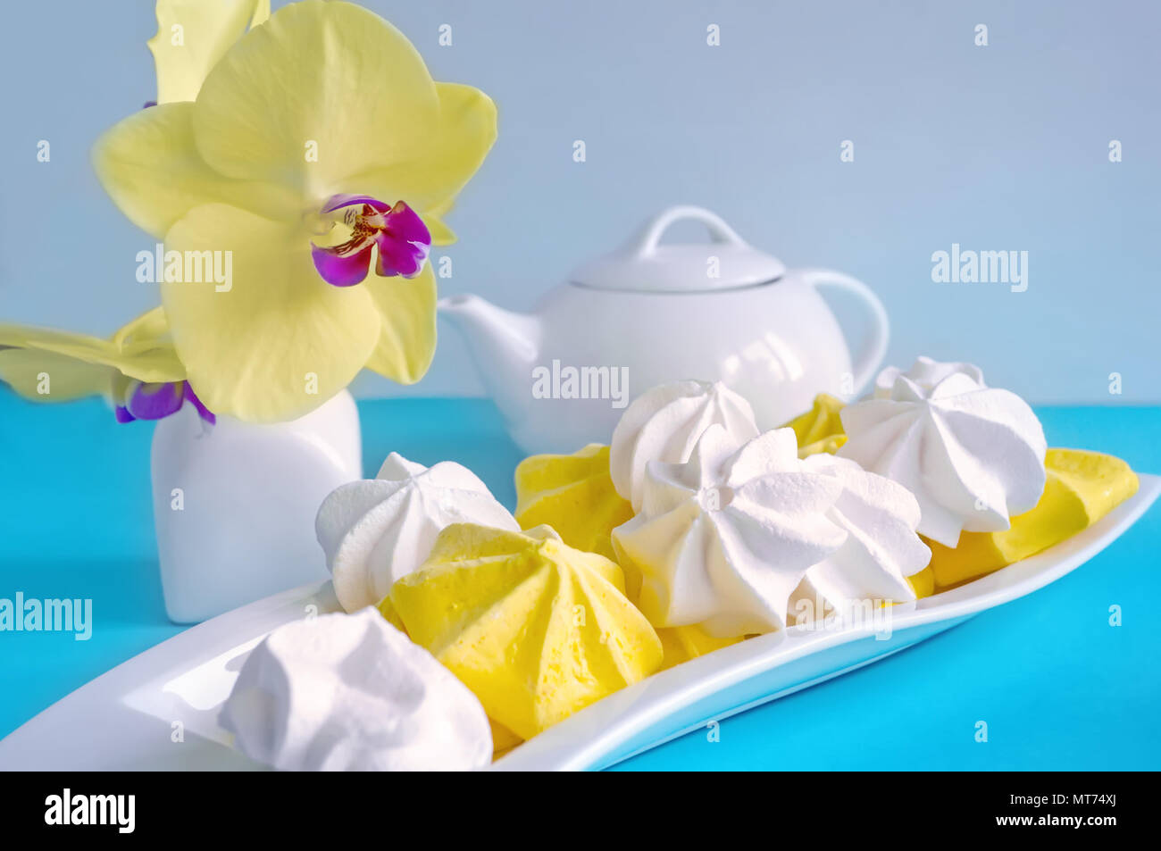 White and yellow meringue on blue background in tea serving with white kettle Stock Photo