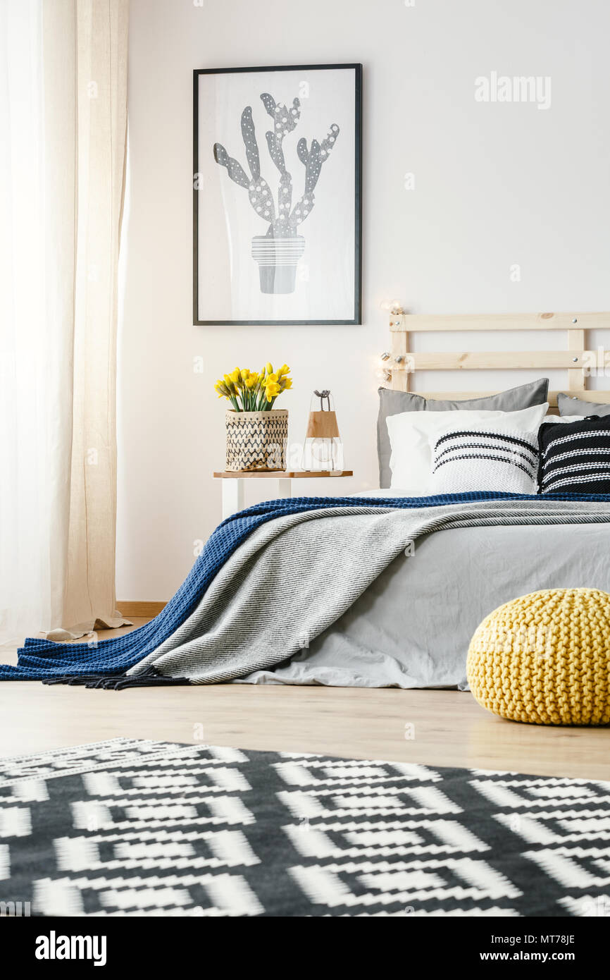 Patterned carpet and yellow pouf in bedroom interior with cactus poster above bed. Real photo Stock Photo