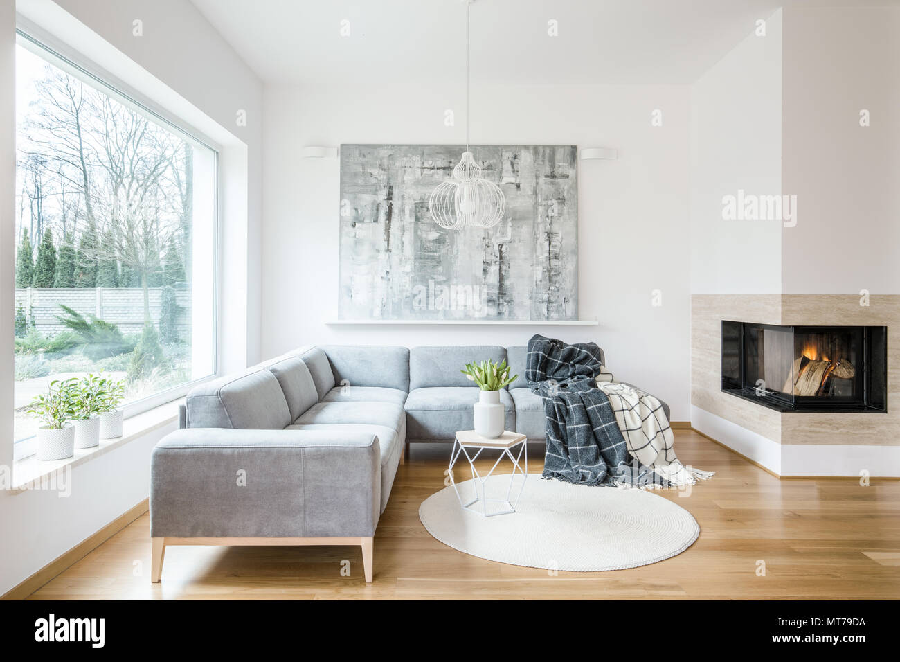 White rug next to a grey corner couch in living room interior with  fireplace and painting Stock Photo - Alamy
